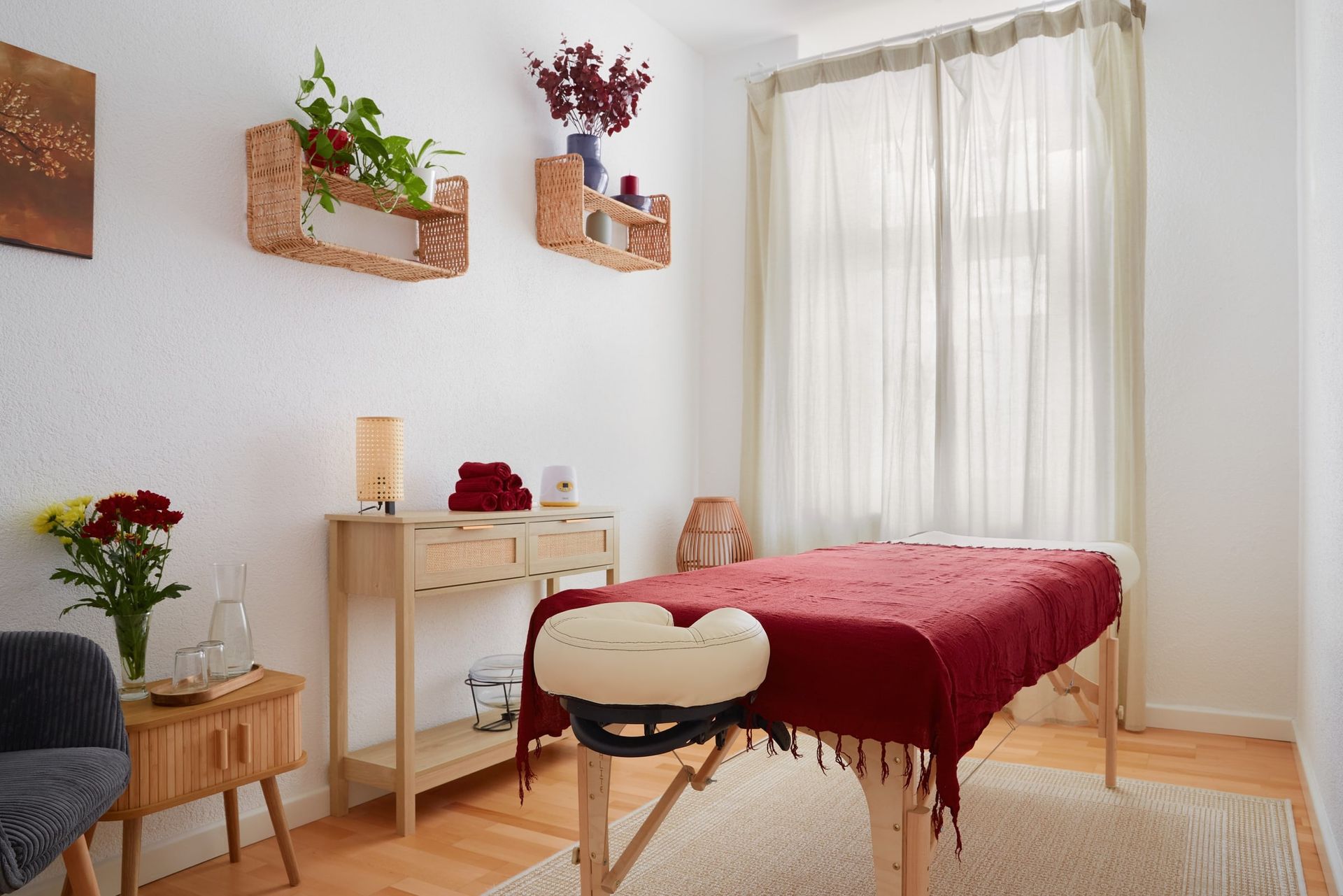 Cozy Room im Harmonie Studio: Massageliege mit rotem Tuch, Holzkonsole mit Handtüchern, Blumen und Tageslicht