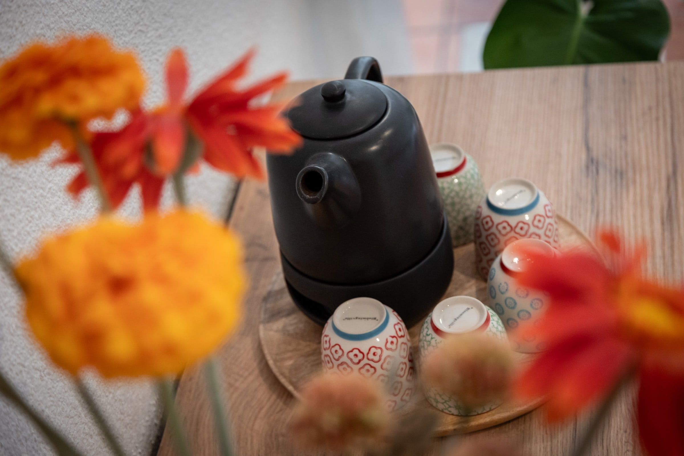 Teekanne und bunte Tassen auf einem Holztablett